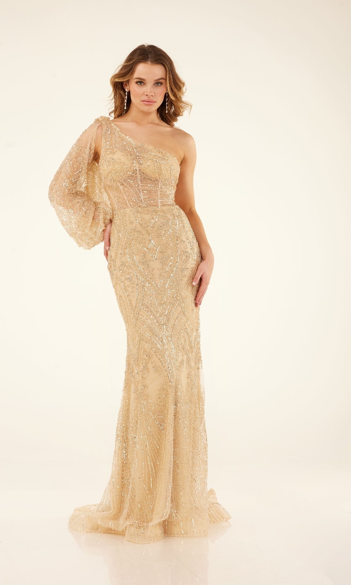 A woman stands against a plain light background wearing the Cecilia Couture C273A, a fitted, floor-length gold one-shoulder prom dress with sparkling sequin embellishments.